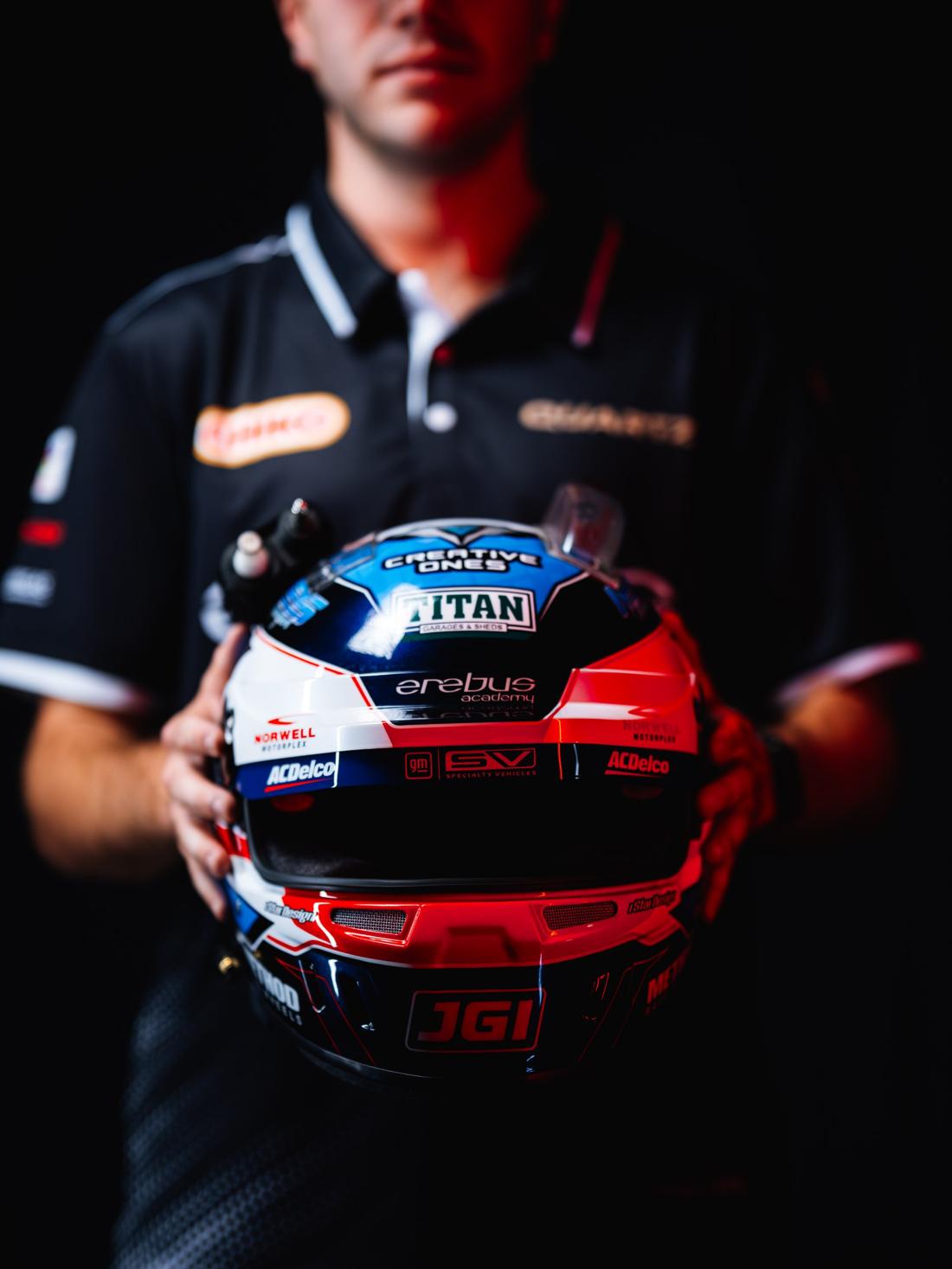 The driver holds his helmet forward, his face blurred in the background